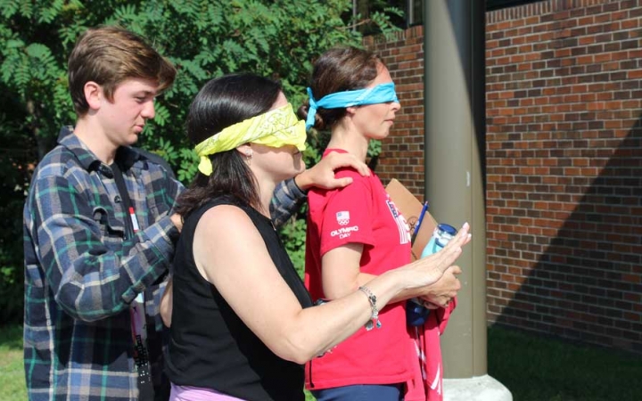 A young person guides two blindfolded people by the shoulders at the family seminar of an outward bound intercept course 